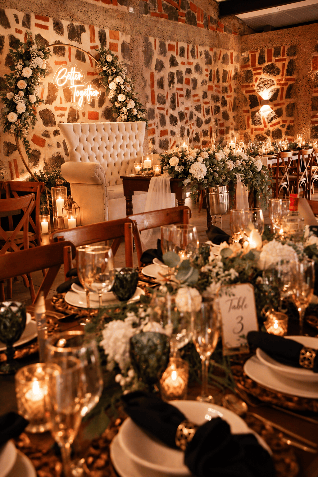Mesas de boda vestidas con velas, arreglos florales y silla de novios frente a muro de piedra