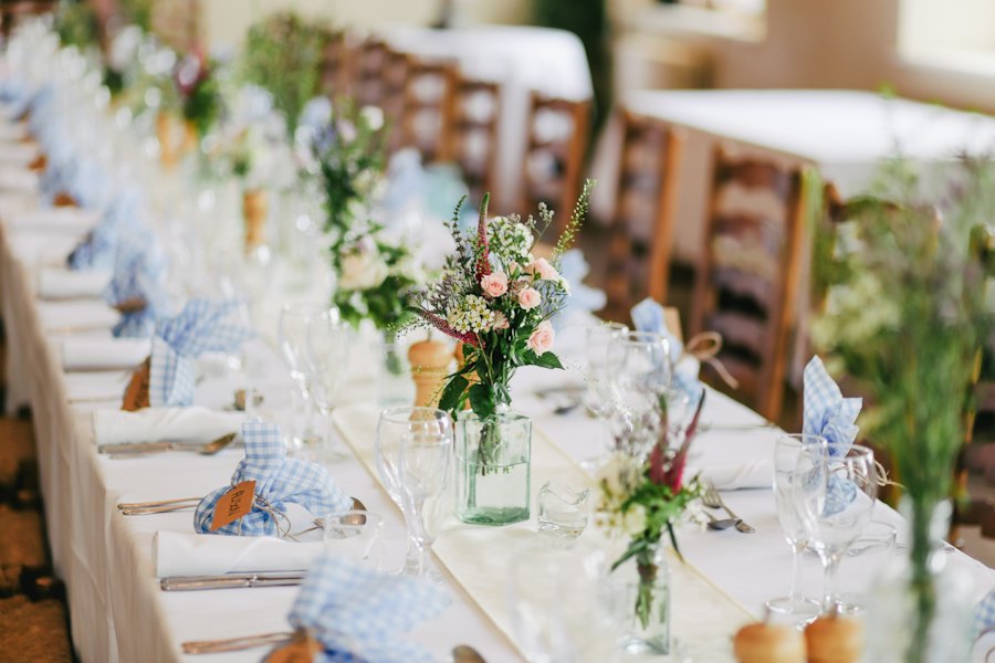 Mesa redonda vestida con mantel blanco, copas y centro de mesa floral