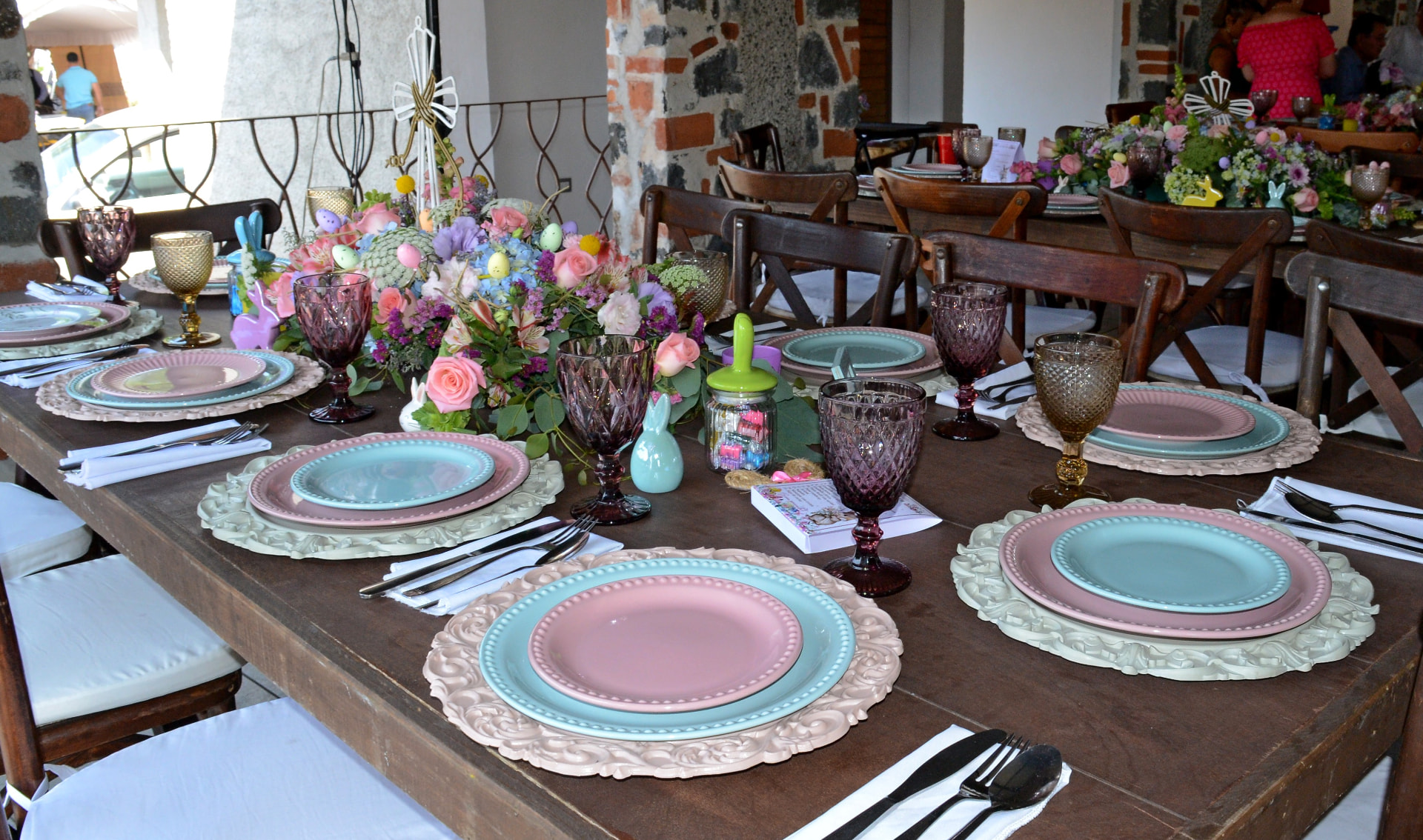Mesa con arreglos florales en tonos pastel, platos de colores y copas