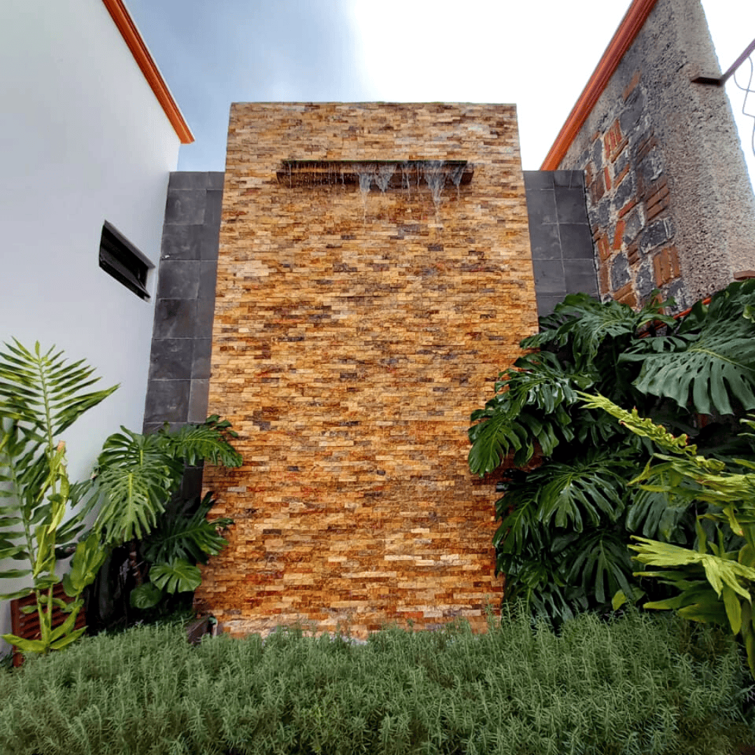 Muro de piedra con cascada de agua entre vegetación en los jardines de Quinta Los Mulatos