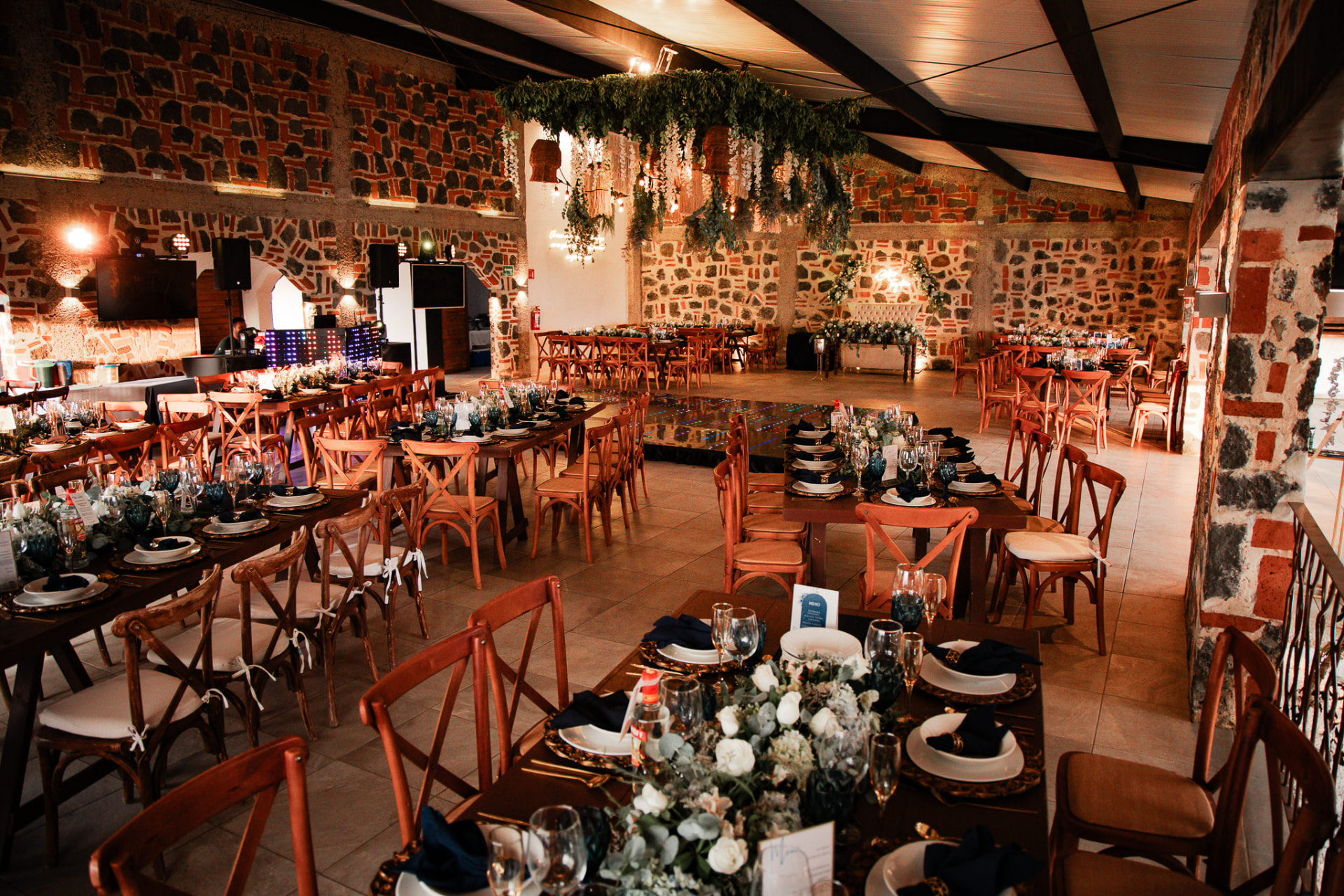 Salón con mesas de madera, sillas cruzadas y montaje de banquete