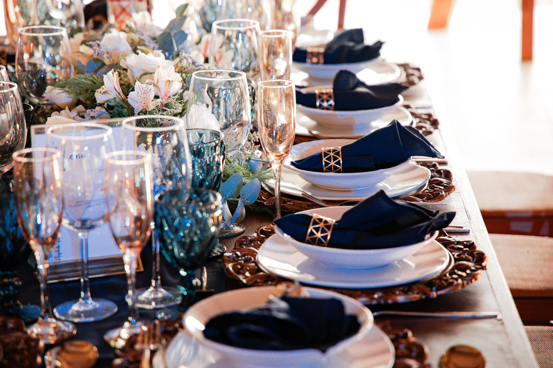 Mesa vestida con loza blanca, cristalería, copas y servilleteros dorados